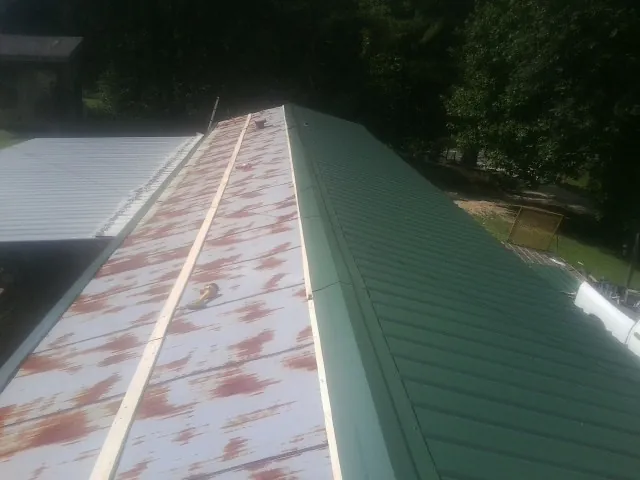 Old rusted panels beside newly installed green metal roofing — Wind Damage Roof Repair by Roofing Brothers in Lomax