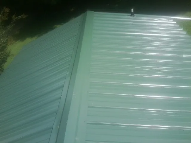 New green metal panels meeting at the ridge of a roof — Flat Roof Repair work by our crew in Lomax