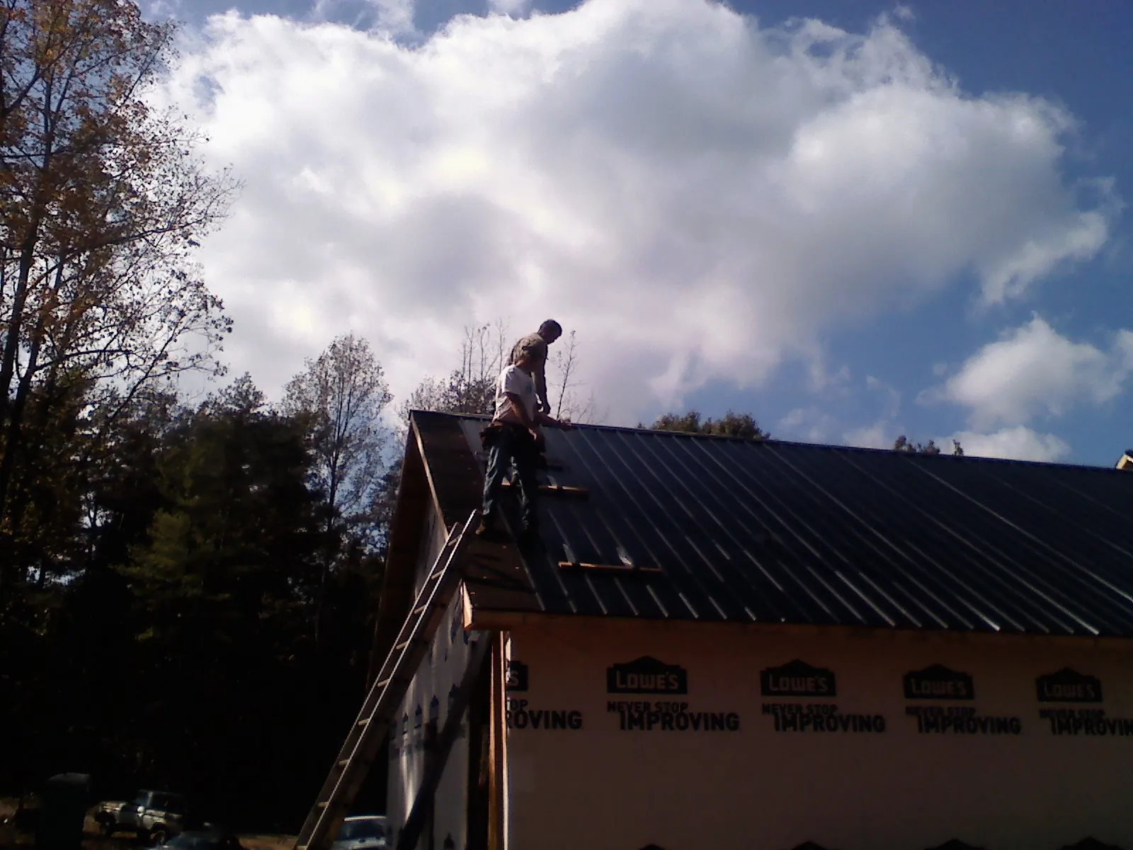 Roofer fastening dark metal panels high against a cloudy sky, from a Roof Inspection job in Lomax