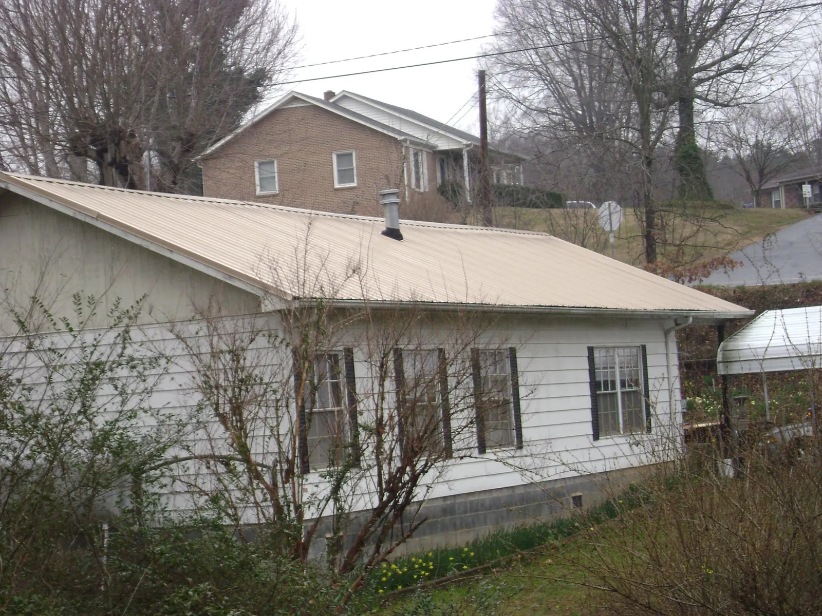 Tan metal roof on a white sided house set into a hillside — Commercial Roofing by Roofing Brothers in Lomax
